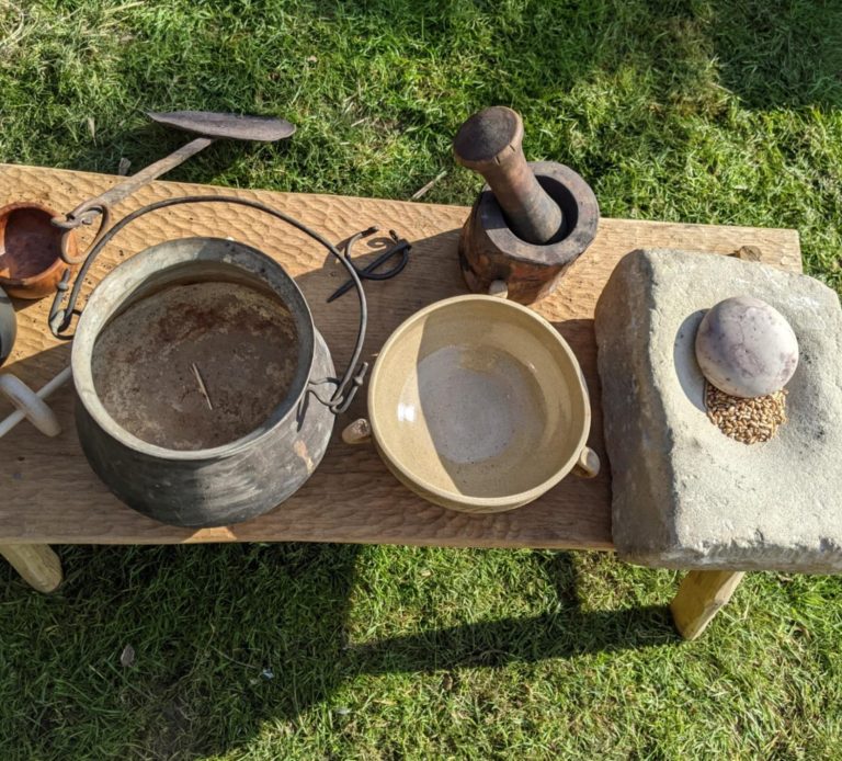 Various historical cooking utensils on a wooden table, including pots and a mortar.